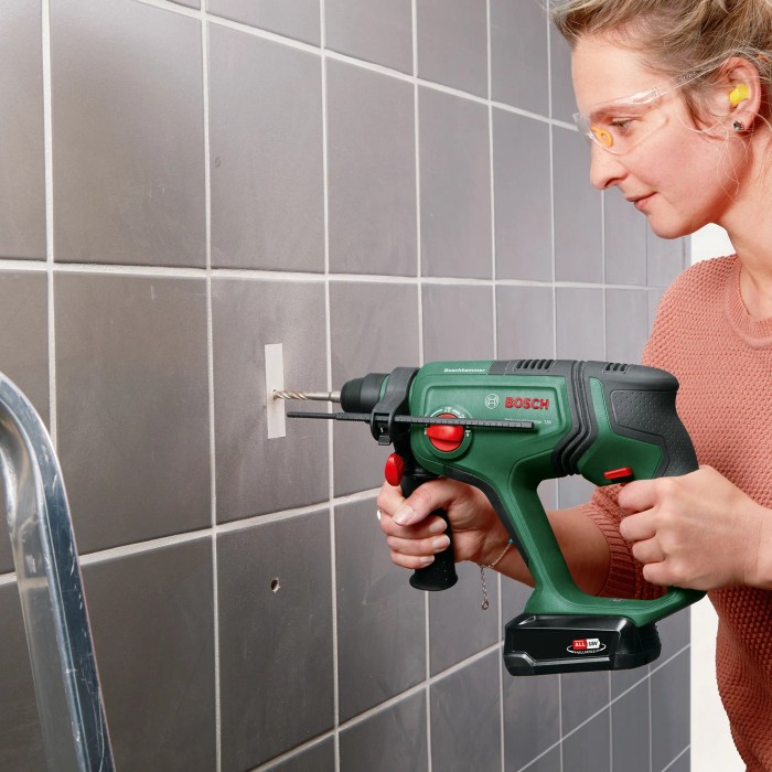 Donna che fora una parete piastrellata con il trapano a percussione a batteria Bosch UniversalHammer 18V.