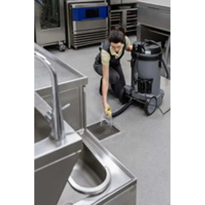 Donna pulisce scarico con aspiratore industriale t.b.t. in cucina in acciaio inox.